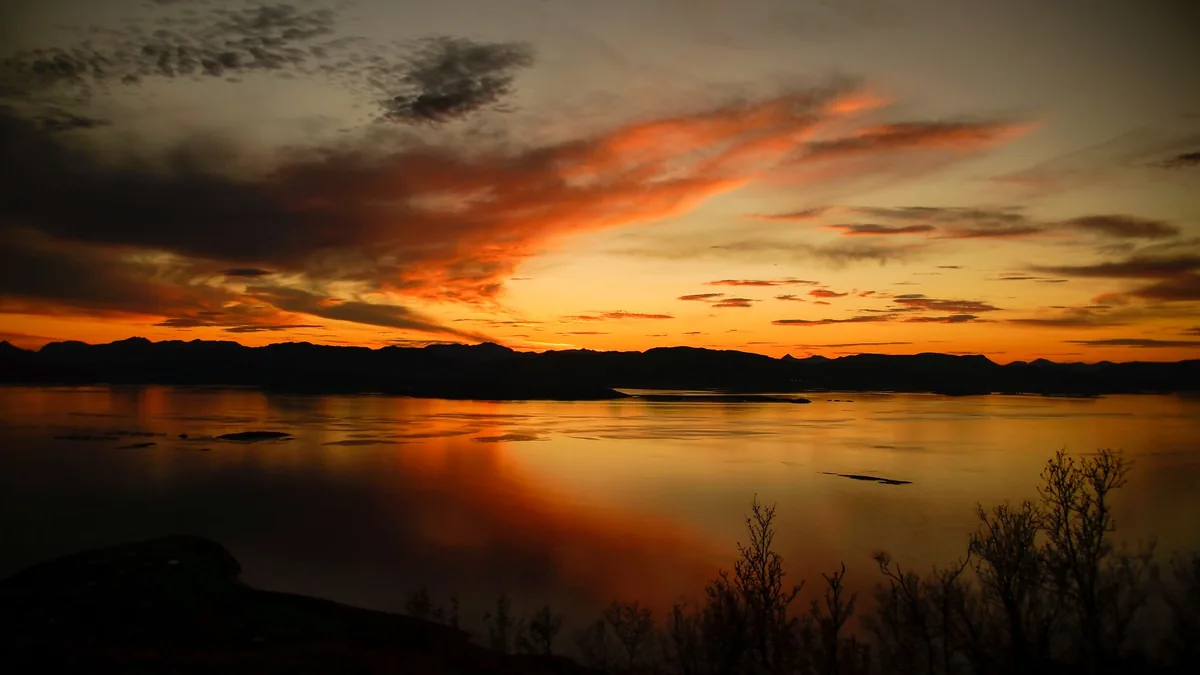 Captivating sunset with dramatic skies reflecting over a serene Norwegian lake.